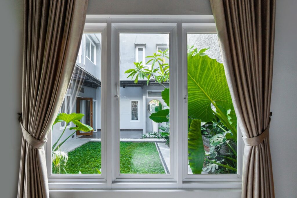 A window with curtains overlooking a green lawn, showcasing different window replacement options