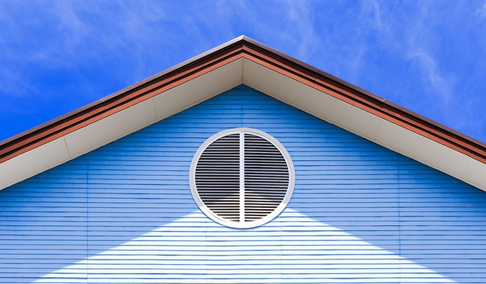 A blue house with a round window and a white roof, displaying different types of home siding